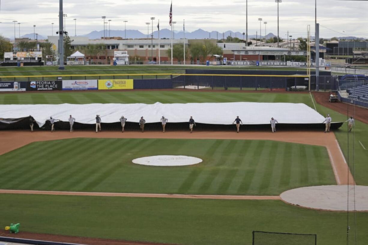 Grounds crew members pull a tarp toward the infield to cover it in anticipation of coming rain after a spring training baseball game between the Los Angeles Angels and the Seattle Mariners Tuesday, March 10, 2020, in Peoria, Ariz.