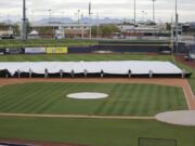 Grounds crew members pull a tarp toward the infield to cover it in anticipation of coming rain after a spring training baseball game between the Los Angeles Angels and the Seattle Mariners Tuesday, March 10, 2020, in Peoria, Ariz.