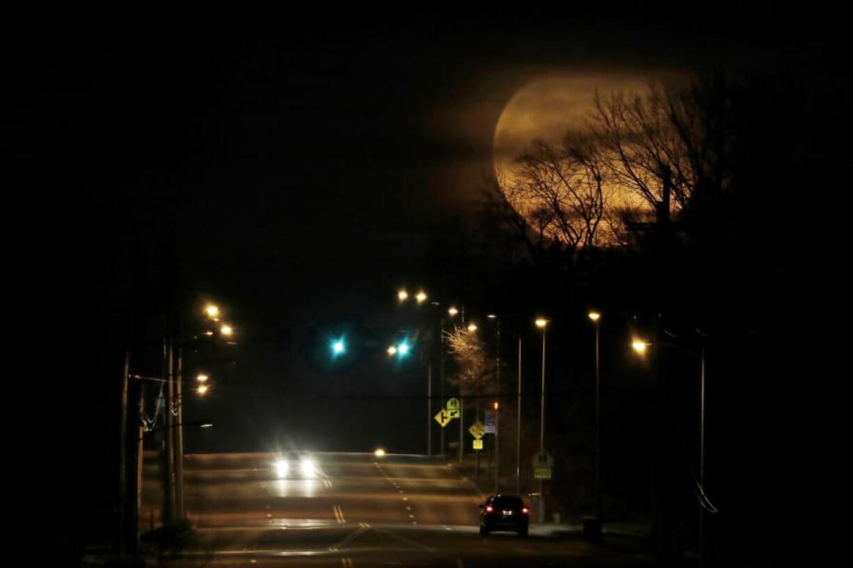 FILE - In this March 10, 2020, file photo, vehicles are dwarfed as the nearly full moon rises in the distance in Shawnee, Kan. The planets and our moon are providing some early morning entertainment. Mars, Jupiter, Saturn and a crescent moon will be clustered together in the southeastern sky just before daybreak. Mercury will peek above the horizon.