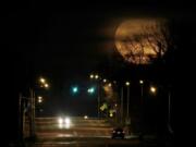 FILE - In this March 10, 2020, file photo, vehicles are dwarfed as the nearly full moon rises in the distance in Shawnee, Kan. The planets and our moon are providing some early morning entertainment. Mars, Jupiter, Saturn and a crescent moon will be clustered together in the southeastern sky just before daybreak. Mercury will peek above the horizon.