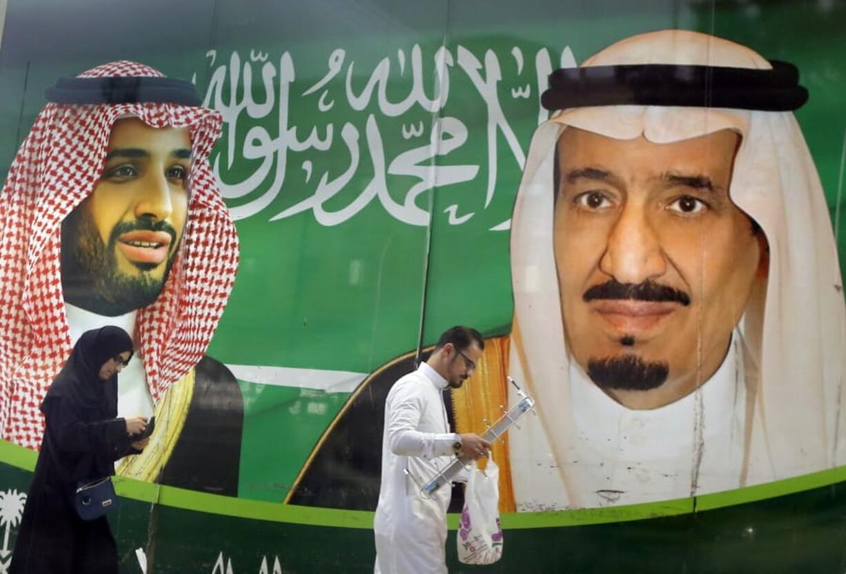 People walk past a banner showing Saudi King Salman, right, and his Crown Prince Mohammed bin Salman, outside a mall in Jiddah, Saudi Arabia, Saturday, March 7, 2020.