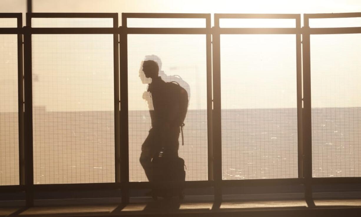 FILE - In this June 26, 2019, file photo a traveller is silhouetted by the setting sun while running past a wind partition in the bus lanes at Denver International Airport in Denver. Whether visiting an exotic destination wedding or just flying back to Cincinnati for your awkward cousin&#039;s nuptials, wedding travel can get expensive in a hurry.