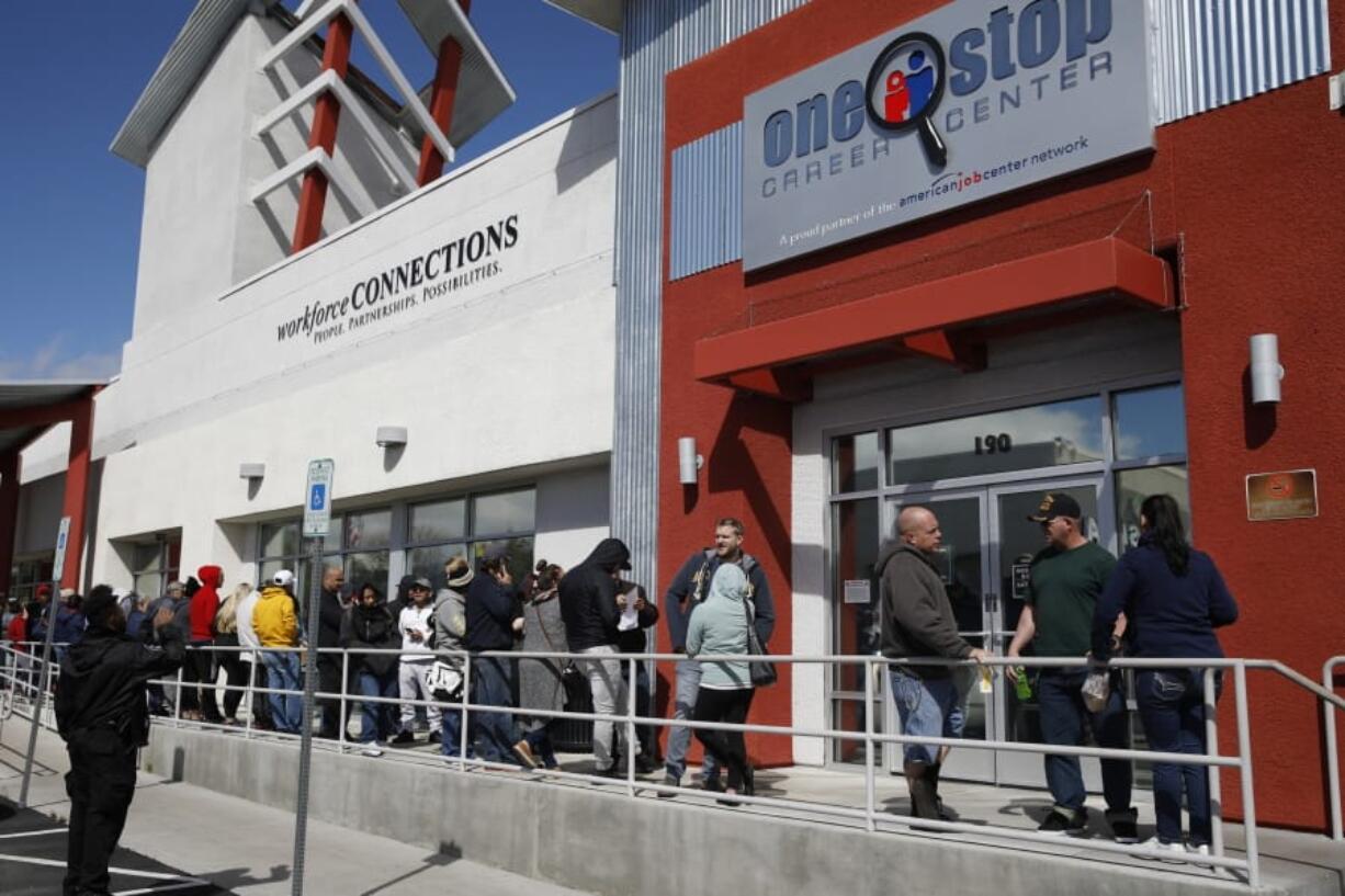 FILE - In this March 17, 2020 file photo, people wait in line for help with unemployment benefits at the One-Stop Career Center in Las Vegas.   A record-high number of people applied for unemployment benefits last week as layoffs engulfed the United States in the face of a near-total economic shutdown caused by the coronavirus. The surge in weekly applications for benefits far exceeded the previous record set in 1982.