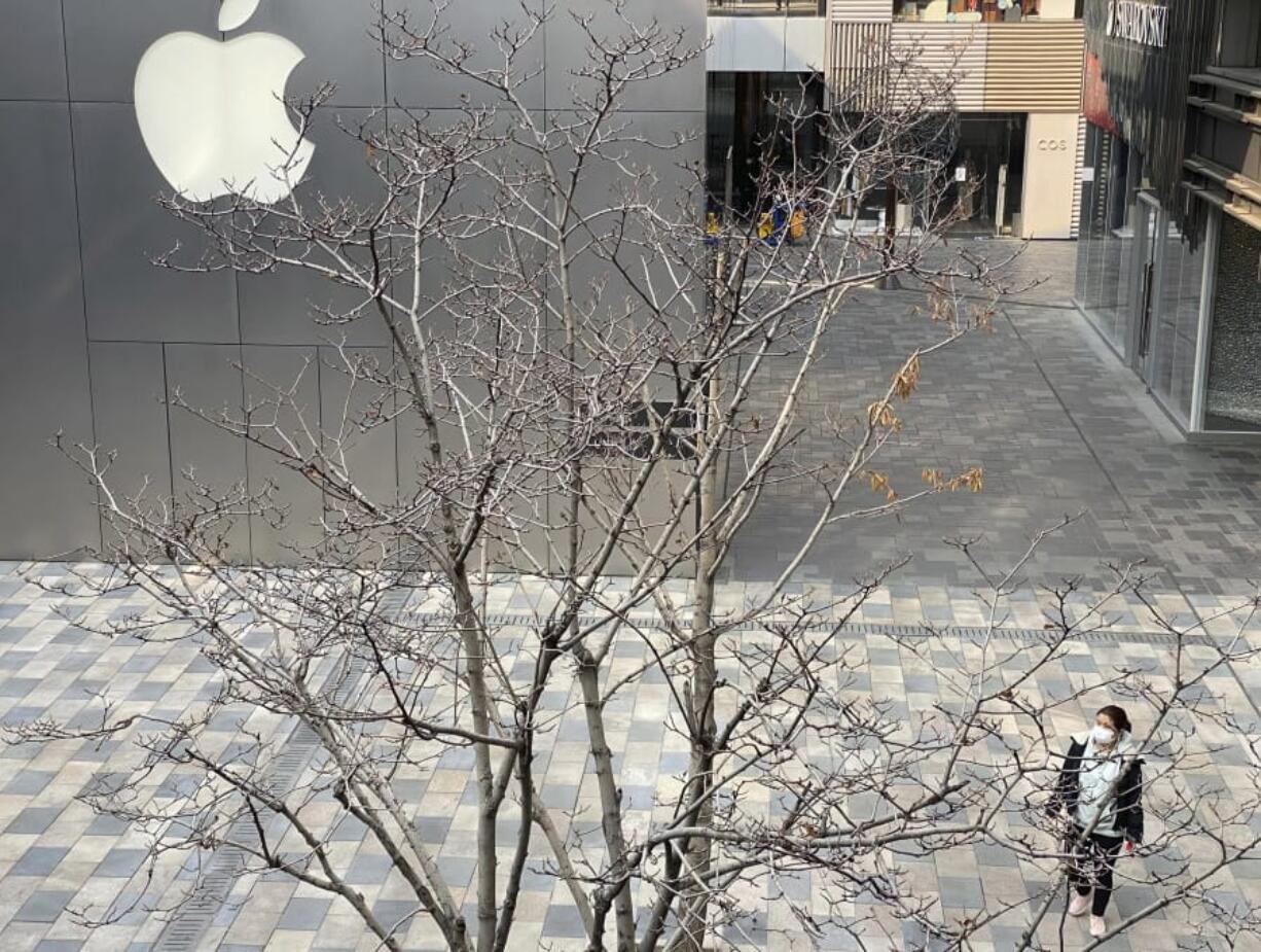 A woman wearing mask walks past the Apple store in an empty mall district in Beijing, China on Wednesday, Feb. 26, 2020. The tech giant Apple has reopened some of its stores in China but says the viral outbreak is starting to disrupt its supplies.