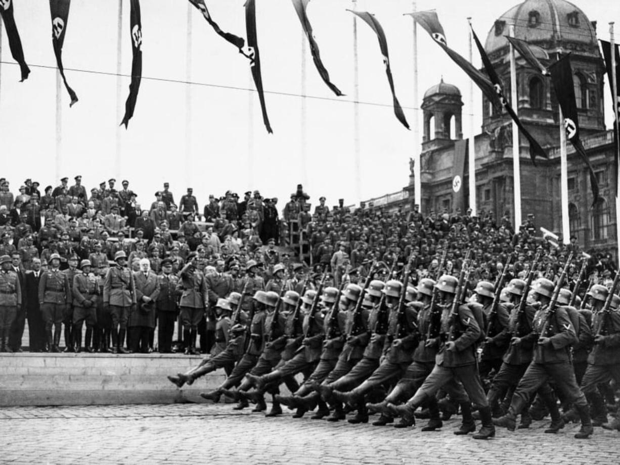 FILE - In this March 24, 1938, file photo, German standard bearers parade past Maj. Gen. Fedor von Bock, commander of all armed forces in the Austrian territory, center, on grandstand on the Kingstrasse in front of the Memorial of Honor, as the troops reach Vienna. Beside him wearing overcoat is Dr. Seysz Incuart. World War II references are now heard daily, not because another momentous 75th anniversary, Victory in Europe Day approaches in May but because of the coronavirus.