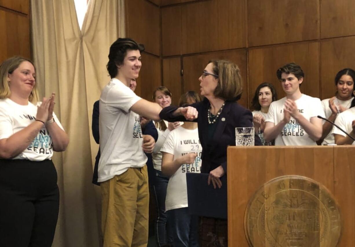 Oregon Gov. Kate brown elbow-bumps student Charlie Abrams at a ceremony on Tuesday, March 10, 2020, where she signed a sweeping executive order for the state to reduce carbon emissions to combat global warming. Amid a spreading coronavirus outbreak, many people are no longer shaking hands and are coming up with alternatives, like the elbow bump.