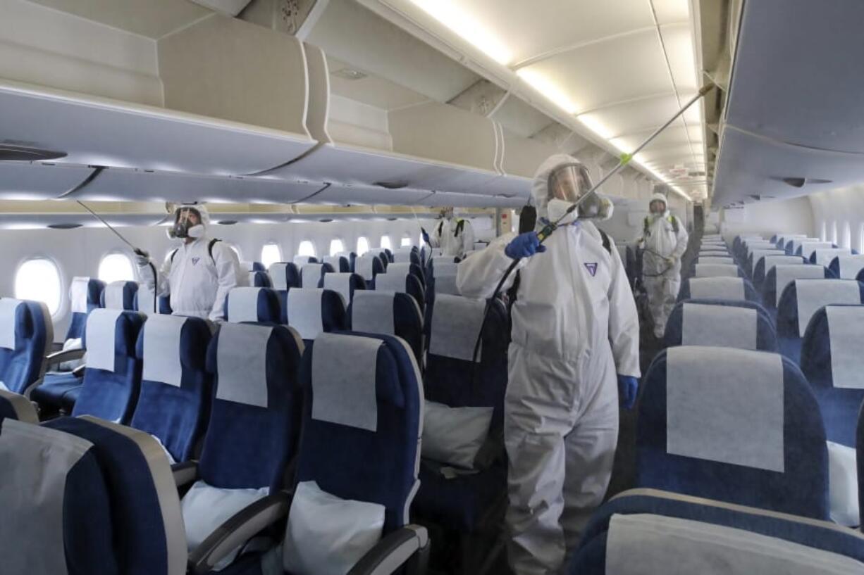 Workers wearing protective gears spray disinfectant inside a plane for New York as a precaution against the new coronavirus at Incheon International Airport in Incheon, South Korea, Wednesday, March 4, 2020. The coronavirus epidemic shifted increasingly westward toward the Middle East, Europe and the United States on Tuesday, with governments taking emergency steps to ease shortages of masks and other supplies for front-line doctors and nurses.