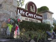 Flowers left next to the sign that marks the entrance to the parking lot of the Life Care Center in Kirkland, Wash. are shown Monday, March 9, 2020, near Seattle. The nursing home is at the center of the outbreak of the COVID-19 coronavirus in Washington state. (AP Photo/Ted S.