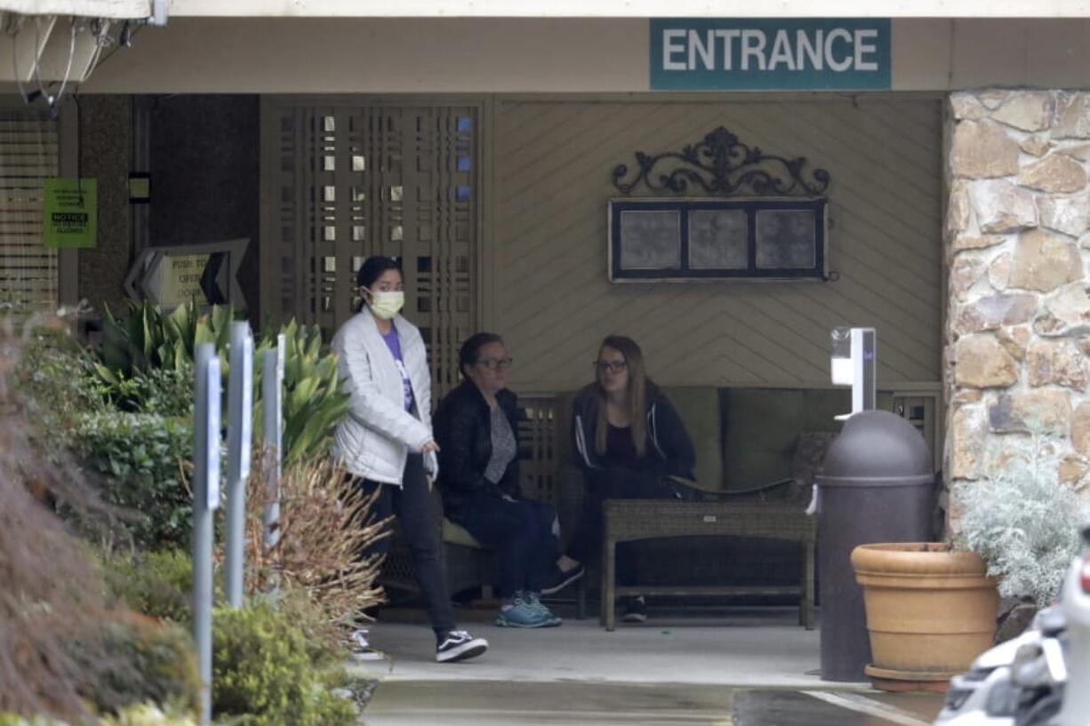 A person wearing a mask walks past a sign banning visitors at the Life Care Center in Kirkland, Wash., near Seattle, Monday, March 2, 2020. Dozens of people associated with the facility are reportedly ill with respiratory symptoms or hospitalized and are being tested for the COVID-19 virus. (AP Photo/Ted S.