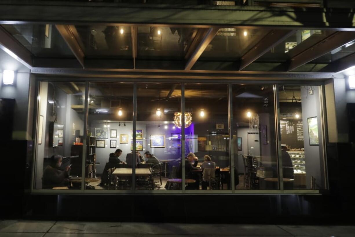 Customers sit in a dining area of Cafe Cosmos in downtown Seattle, Sunday, March 15, 2020. Washington Gov. Jay Inslee said Sunday night that he would order all bars, restaurants, entertainment and recreation facilities in the state to temporarily close to fight the spread of the COVID-19 coronavirus. Inslee said that restaurants could continue take-out and delivery services, the owner of the cafe said he would continue to offer take-out coffee and other food. (AP Photo/Ted S.