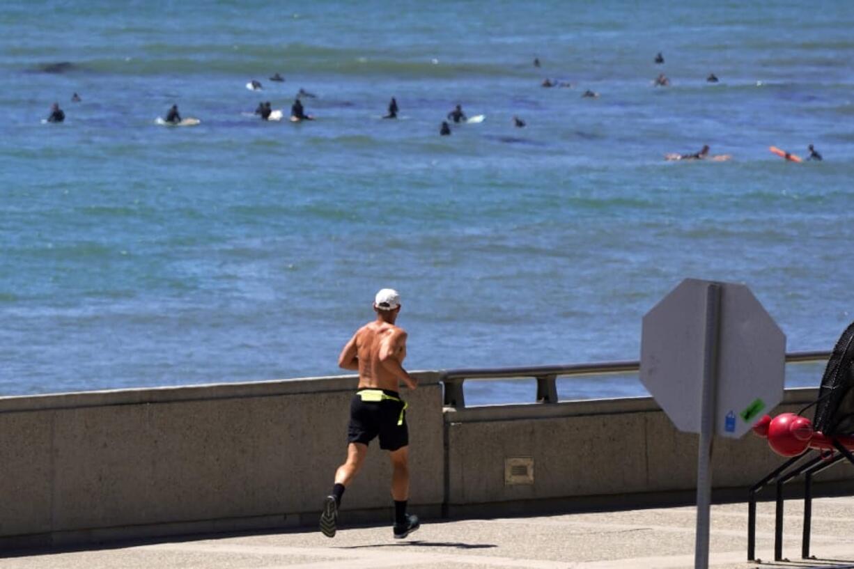 A jogger runs along a path Thursday as surfers are seen in the background in Ventura, Calif. (mark j.