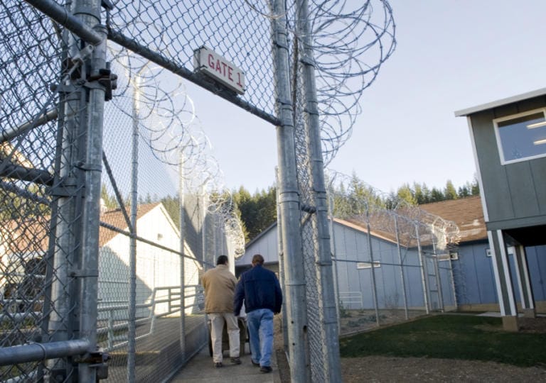 An inmate and guard walk through a gate at Larch Corrections Center in December 2009.