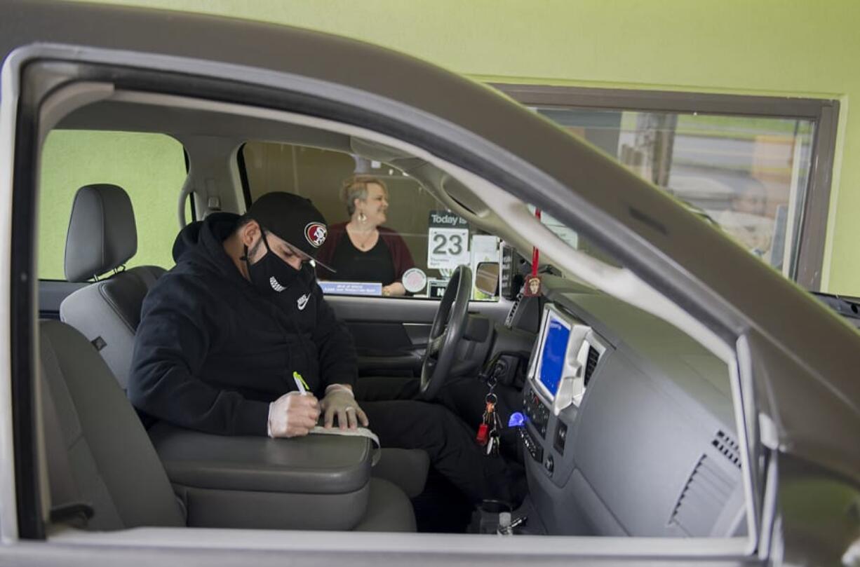 Vancouver resident Ruben Renteria, foreground, checks out his receipt while teller Melissa Engler looks on as he stops by the Cascade Park Columbia Credit Union Branch drive-thru Thursday afternoon. Banks are still allowed to operate during the COVID-19 pandemic, but most are using drive-thru and appointment-only service.