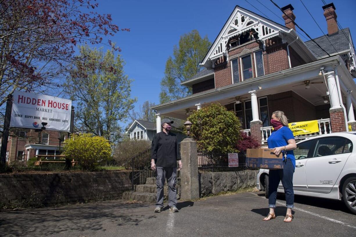 David White, co-owner of Hidden House Market, greets customer Jennifer Calvery of Vancouver as she picks up her takeout order Thursday morning. The restaurant is still serving takeout food, as well as curbside grocery pickup.