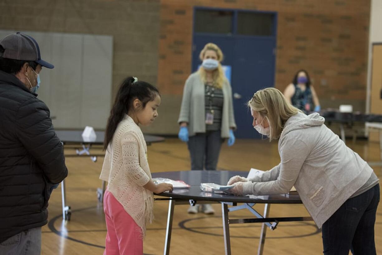 Eduardo Garcia, from left, looks on as his daughter, second-grade student Jaqueline Garcia Reyes, 8, picks up educational materials from writing teacher Tricia Judkins at Washington Elementary School on Monday morning. Vancouver Public Schools delivered iPads to kindergarten through second-grade students this week.