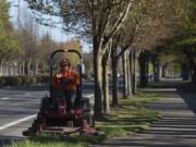 Storme Telford of the Vancouver Public Works department trims grass along Southeast 192nd Avenue on Tuesday morning. Vancouver has resumed some nonemergency public works operations, like mowing and street sweeping. Telford was given a protective mask but said she was not using it because she was away from people.