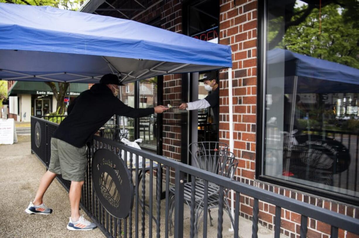 Bart Disher of Camas, left, hands his payment to Paul Le, co-owner of The Sushi Joint, as he picks up a takeout order in Camas. Le set up a table outside the restaurant patio for customers to pick up their orders while maintaining a safe social distance.