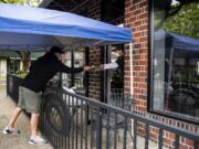 Bart Disher of Camas, left, hands his payment to Paul Le, co-owner of The Sushi Joint, as he picks up a takeout order in Camas. Le set up a table outside the restaurant patio for customers to pick up their orders while maintaining a safe social distance.