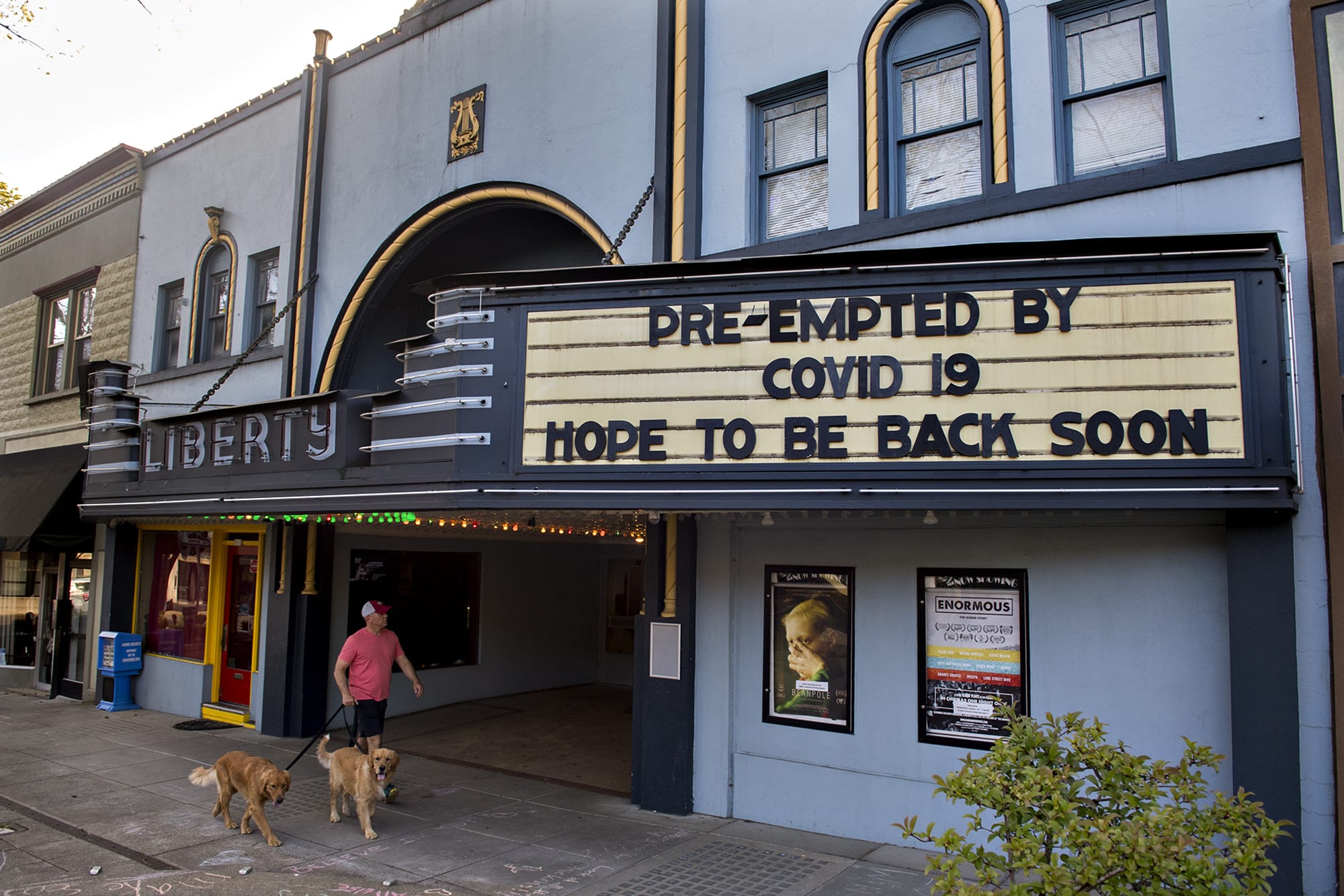 Chuck Nadgwick of Camas passes the historic Liberty Theatre, which is currently closed during the COVID-19 quarantine, as he enjoys a warm spring evening with his dogs Friday, April 17, 2020. Nadgwick was on his way to get takeout at a restaurant downtown but found there wasn't the usual bustling Friday night foot traffic due to closures from the coronavirus. "It's amazing how quiet it is," he said.