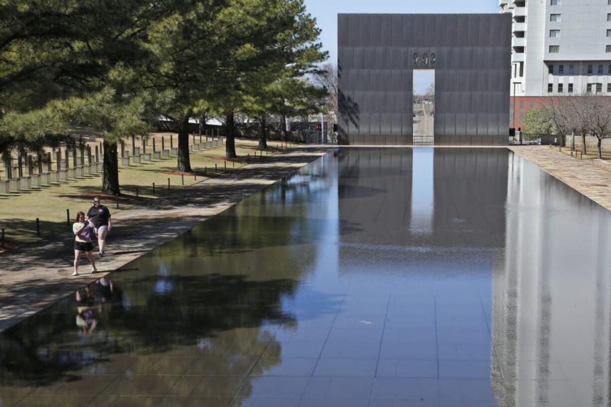 FILE - In this March 18, 2020 file photo, visitors walk next to the reflecting pool at the Oklahoma City National Memorial and Museum in Oklahoma City. The Oklahoma City National Memorial and Museum has announced that it will offer a recorded, one-hour television program in place of a live ceremony to mark the 25th anniversary of the Oklahoma City bombing due to concerns about the spread of the coronavirus.