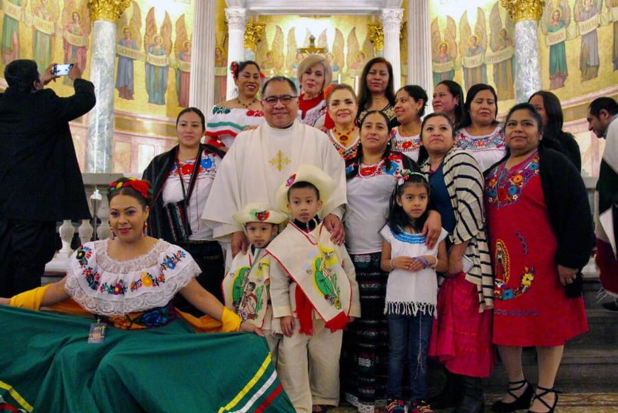 In this Dec. 7, 2019 photo provided by The Tablet, the Rev. Jorge Ortiz-Garay stands with congregants during a Migration Day Mass at St. Brigid Church in the Brooklyn borough of New York.  Ortiz-Garay died on March 27, 2020, from coronavirus-related complications and is now the first known priest in the U.S. to have died from the virus.