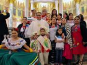 In this Dec. 7, 2019 photo provided by The Tablet, the Rev. Jorge Ortiz-Garay stands with congregants during a Migration Day Mass at St. Brigid Church in the Brooklyn borough of New York.  Ortiz-Garay died on March 27, 2020, from coronavirus-related complications and is now the first known priest in the U.S. to have died from the virus.