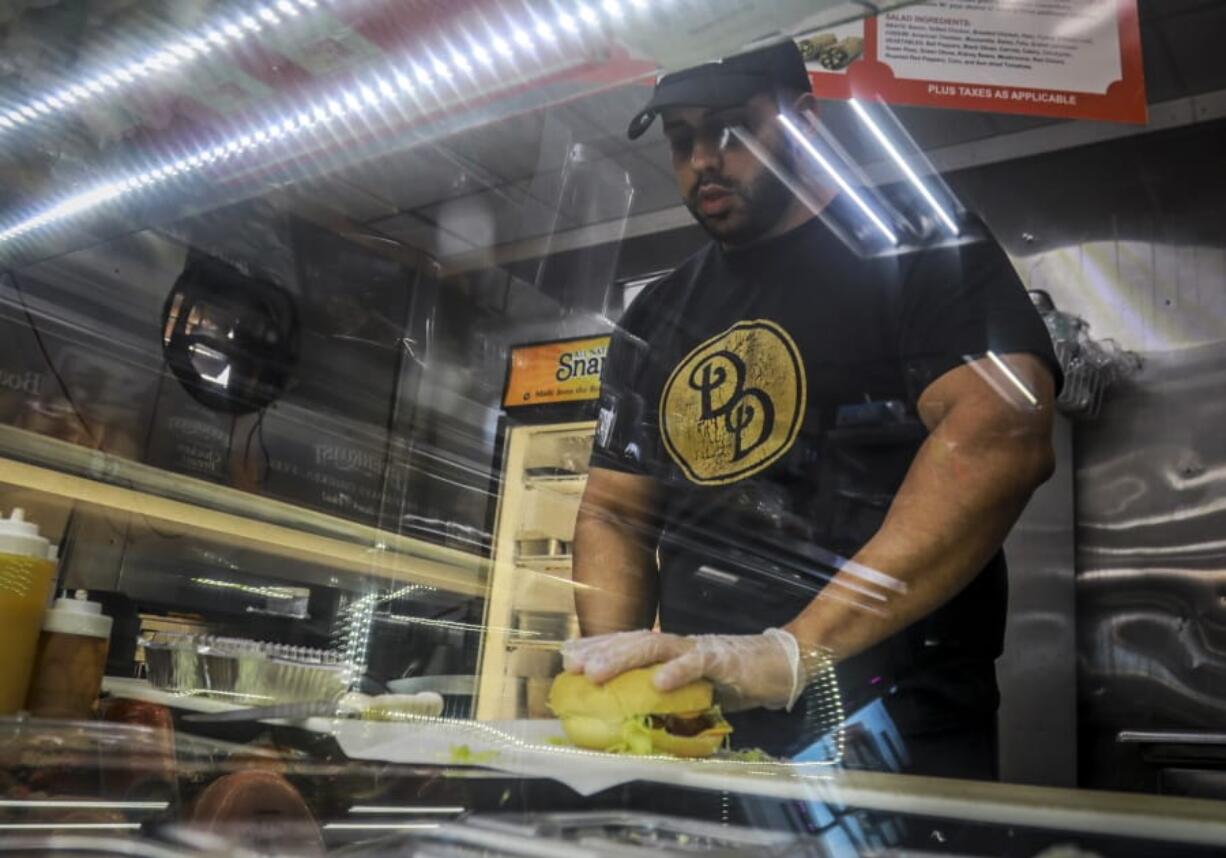 Alex Batista, co-owner of Deli-licious delicatessen in the Queens borough of New York, April 6, 2020, makes a sandwich at the store. In the days of coronavirus and sheltering in place, &quot;it&#039;s been a ghost town,&quot; Batista said.