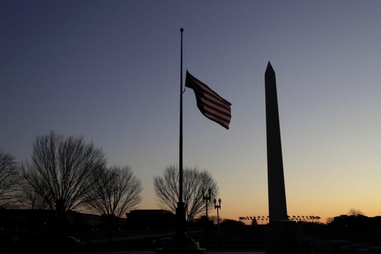 FILE - In this Thursday, Dec. 19, 2019 file photo, a flag at the World War II Memorial flies upside down after it unclipped from its snaphook, before sunrise on Capitol Hill in Washington. At right is the Washington Monument.