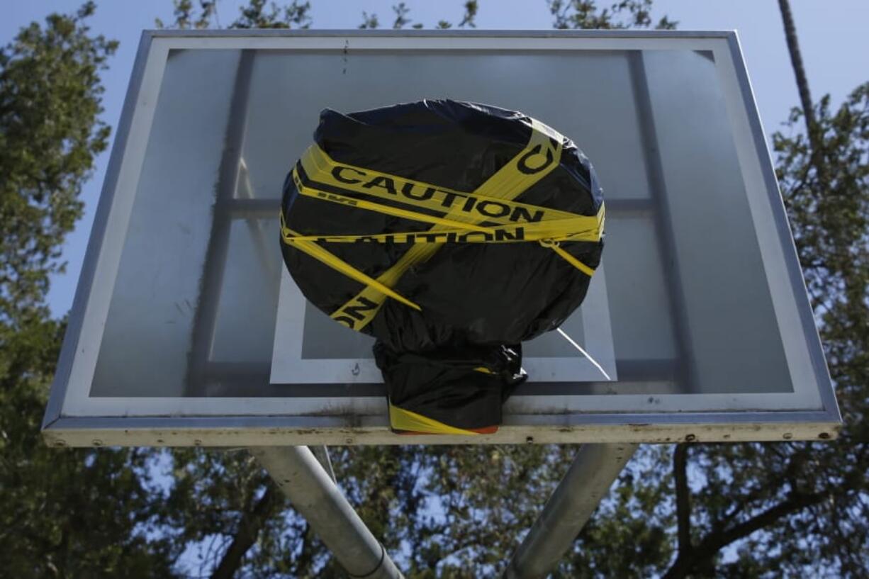 Yellow caution tape and a plastic tarp cover a basketball rim at McKinley Park in Sacramento, Calif., Tuesday, April 21, 2020. The park remains open but the rims were covered because people were not following social distancing rules in place due to the coronavirus outbreak.