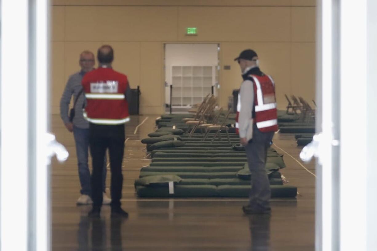 A group of officials stand in front of beds at Moscone West in San Francisco, Thursday, April 2, 2020. Since the beginning of the international pandemic, officials in California have said one population is particularly vulnerable to contracting the coronavirus and spreading it to others: the homeless. Officials are setting up 400 beds at the Moscone Center to house homeless people who are currently in shelters to allow for more social distancing.