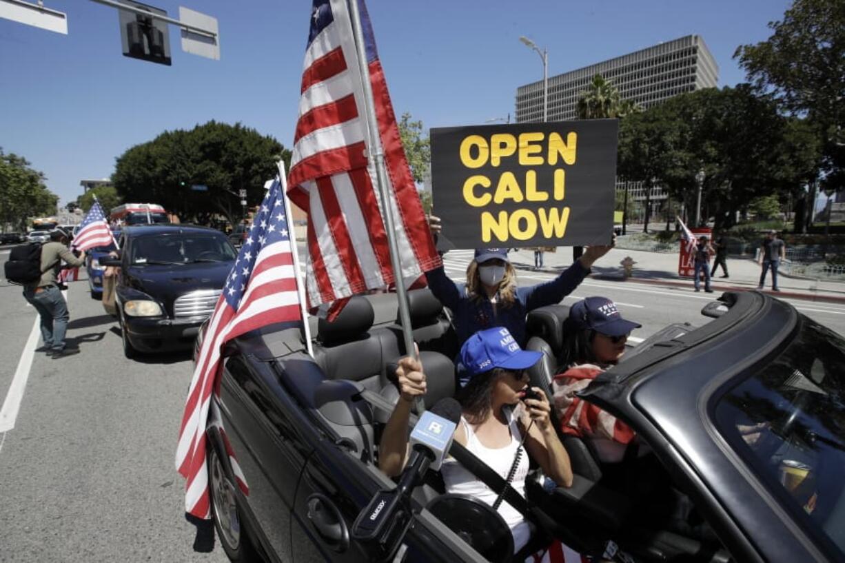 Protesters drive by in a convertible car during a rally calling for an end to California Gov. Gavin Newsom&#039;s stay-at-home orders amid the COVID-19 pandemic, Wednesday, April 22, 2020, outside of City Hall in downtown Los Angeles.