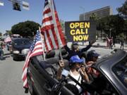 Protesters drive by in a convertible car during a rally calling for an end to California Gov. Gavin Newsom&#039;s stay-at-home orders amid the COVID-19 pandemic, Wednesday, April 22, 2020, outside of City Hall in downtown Los Angeles.