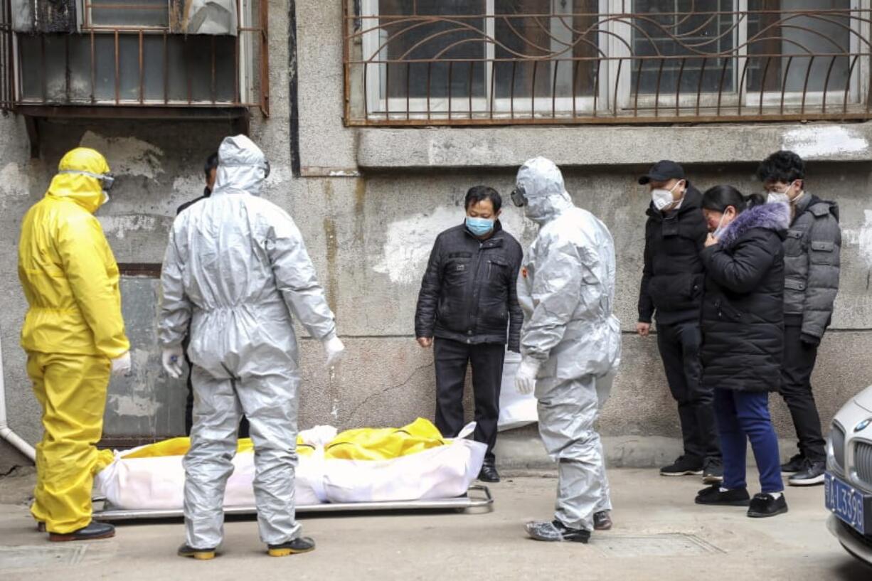 FILE - In this Feb. 1, 2020, file photo, funeral home workers remove the body of a person suspected to have died from the coronavirus outbreak from a residential building in Wuhan in central China&#039;s Hubei Province. The central Chinese city of Wuhan has raised its number of COVID-19 fatalities by more than 1,000. State media said the undercount had been due to the insufficient admission capabilities at overwhelmed medical facilities at the peak of the outbreak.