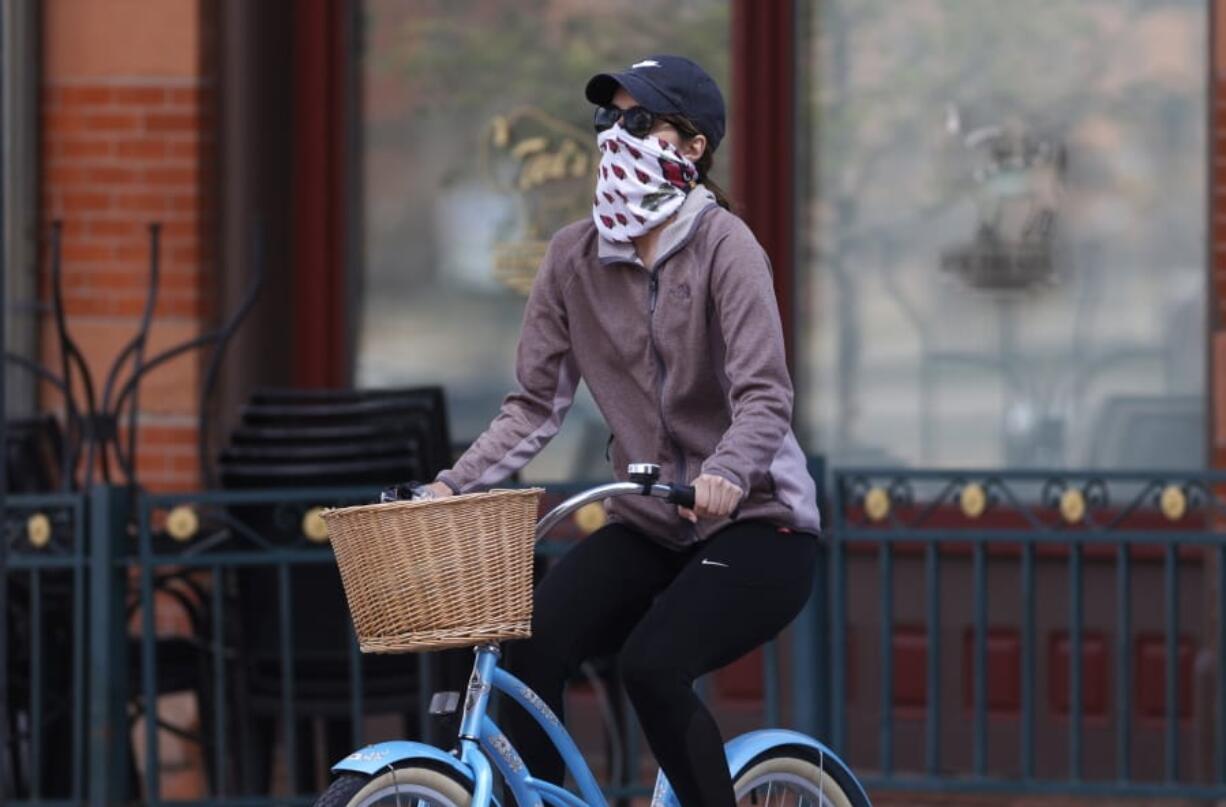 A bicyclist wears face protection against the new coronavirus while pedaling through Larimer Square early Saturday, April 25, 2020, in downtown Denver.