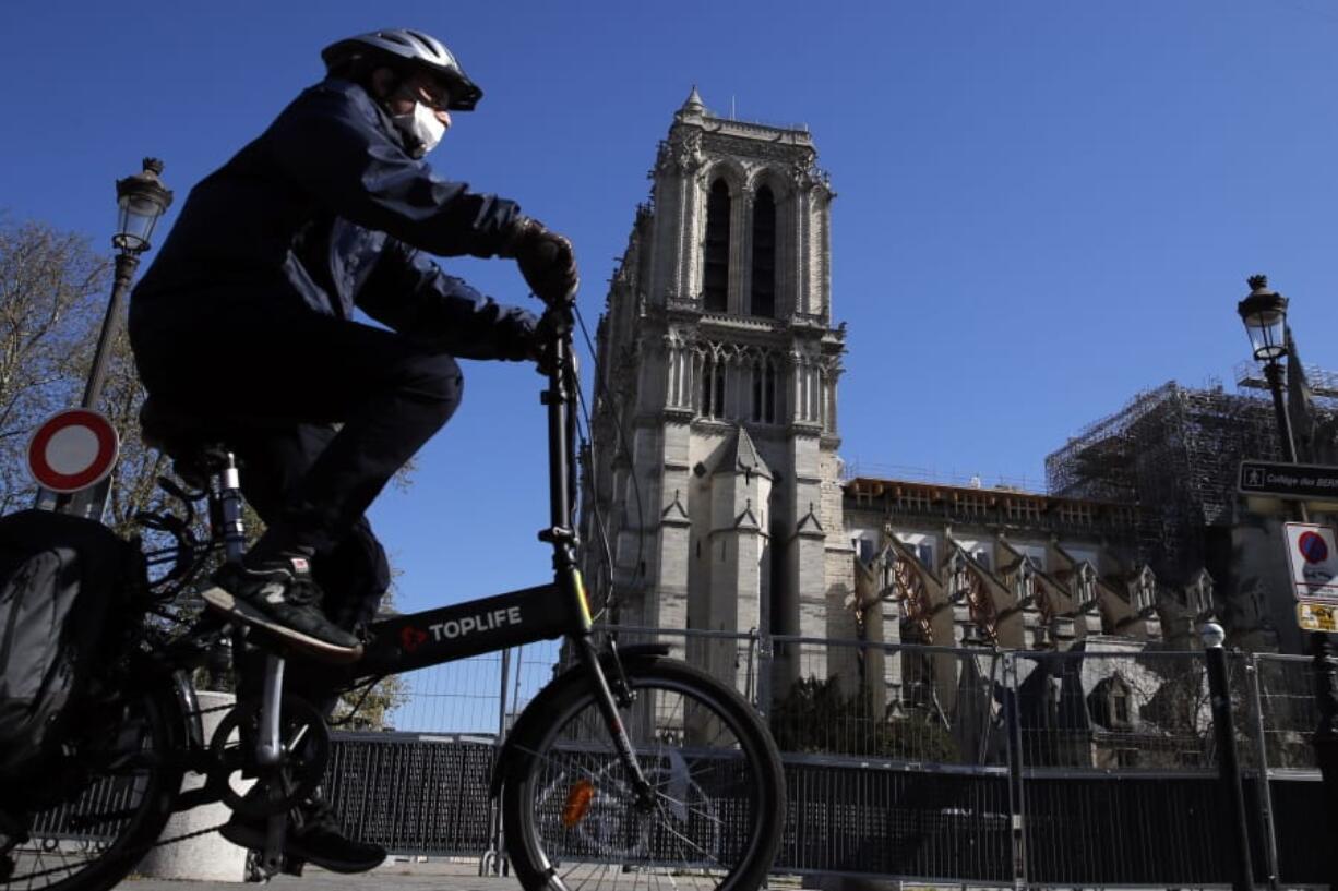 A man wearing a face mask rides his bike in front of Notre Dame cathedral during a nationwide confinement to counter the Covid-19, in Paris, Sunday, April 5, 2020. The new coronavirus causes mild or moderate symptoms for most people, but for some, especially older adults and people with existing health problems, it can cause more severe illness or death.