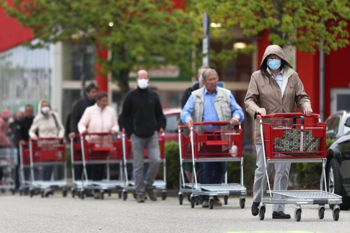 People wearing protective masks queue up to go in a garden store in Munich, Germany, Monday, April 20, 2020. The German government has moved to restrict freedom of movement for people, in an effort to slow the onset of the COVID-19 coronavirus.