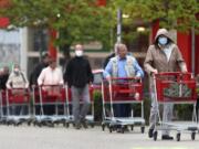 People wearing protective masks queue up to go in a garden store in Munich, Germany, Monday, April 20, 2020. The German government has moved to restrict freedom of movement for people, in an effort to slow the onset of the COVID-19 coronavirus.