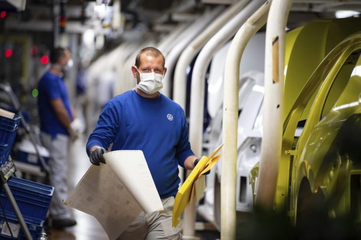 An employee walks past vehicles in production with a face mask in the VW plant in Wolfsburg, Germany, Monday, April 27, 2020. Volkswagen is gradually launch the production at important plants after the corona lockdown.