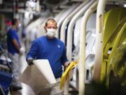 An employee walks past vehicles in production with a face mask in the VW plant in Wolfsburg, Germany, Monday, April 27, 2020. Volkswagen is gradually launch the production at important plants after the corona lockdown.