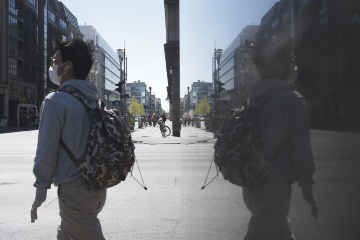 A man with a face mask walks over the Friedrichstrasse, a main shopping street, in Berlin, Germany, Wednesday, April 22, 2020. Smaller shops allowed to open in the German capital from today on.