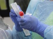 A nurse holds a vial and a swab at a drive-up coronavirus testing station at a hospital in Seattle.  (AP Photo/Ted S.