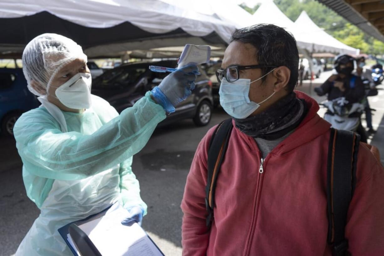 A health workers checks the temperature of a man during COVID-19 coronavirus testing Thursday, April 23, 2020, in Gombak on the outskirts of Kuala Lumpur, Malaysia. The Malaysian government issued a restricted movement order to the public for the rest of the month to help curb the spread of the new coronavirus.