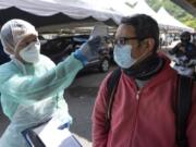 A health workers checks the temperature of a man during COVID-19 coronavirus testing Thursday, April 23, 2020, in Gombak on the outskirts of Kuala Lumpur, Malaysia. The Malaysian government issued a restricted movement order to the public for the rest of the month to help curb the spread of the new coronavirus.