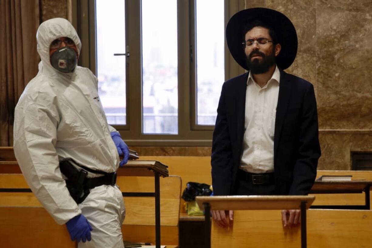 An Israeli police officer wearing protective gear waits to detain an ultra-Orthodox man as he prays in a synagogue because of the government&#039;s measures to help stop the spread of the coronavirus, in Bnei Brak, a suburb of Tel Aviv, Israel, Thursday, April 2, 2020. ?On Wednesday, Israeli Prime Minister Benjamin Netanyahu ordered a police cordon around the largely ultra-Orthodox city of Bnei Brak, to limit movement to and from the city. Bnei Brak has the second highest number of coronavirus cases in Israel.