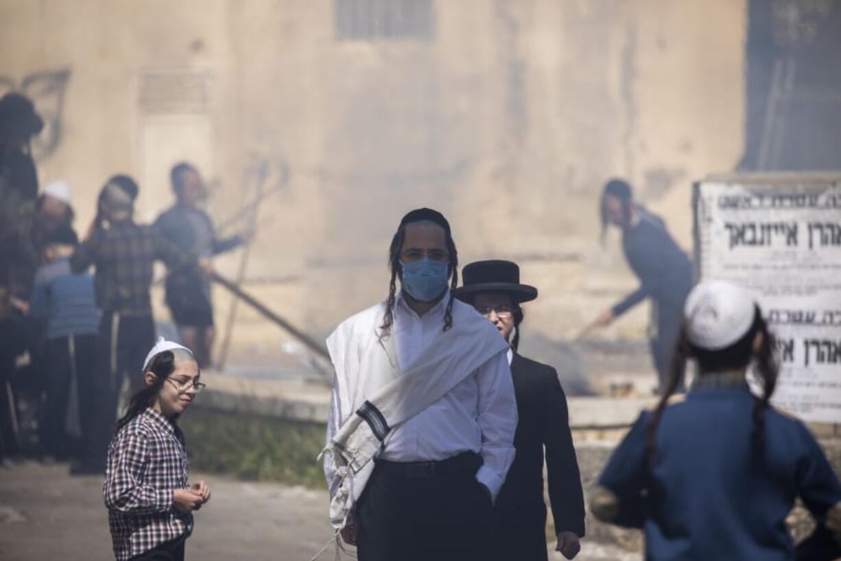 An ultra-Orthodox Jewish men wears a face mask as children burn leavened items in final preparation for the Passover holiday in the Orthodox neighborhood of Mea Shearim in Jerusalem, Wednesday, April 8, 2020. Jerusalem authorities have said they will gather the bread and burn it in a big bonfire in one location to avoid large gatherings. But, some in the Mea Shearim neighborhood shunned the orders.