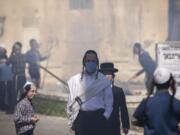 An ultra-Orthodox Jewish men wears a face mask as children burn leavened items in final preparation for the Passover holiday in the Orthodox neighborhood of Mea Shearim in Jerusalem, Wednesday, April 8, 2020. Jerusalem authorities have said they will gather the bread and burn it in a big bonfire in one location to avoid large gatherings. But, some in the Mea Shearim neighborhood shunned the orders.