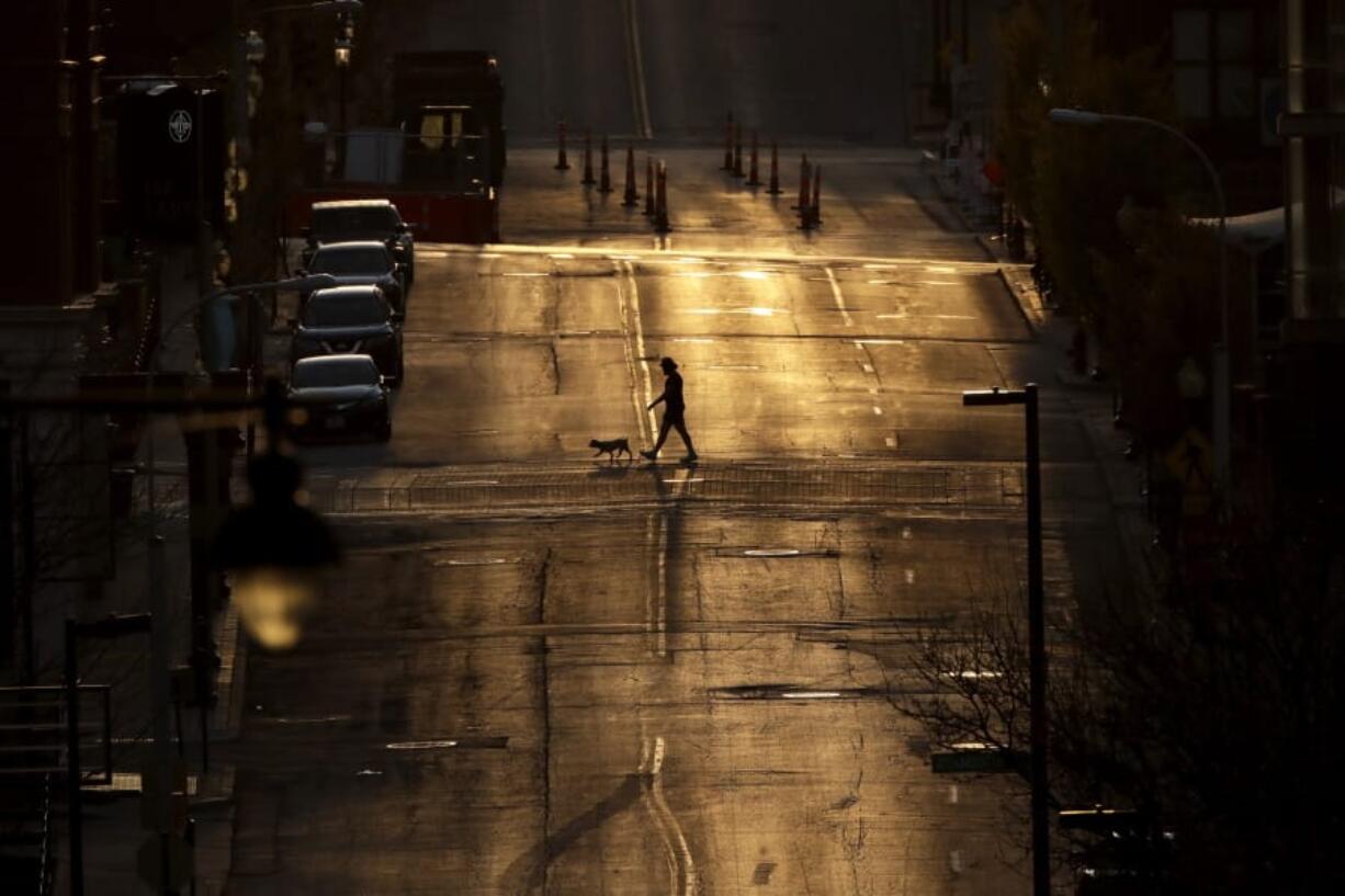 A man walks a dog on an empty downtown street as the sun sets Wednesday, April 1, 2020, in Kansas City, Mo.