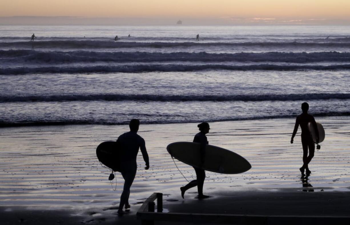 Surfers prepare to enter the water at Sumner Beach as level four COVID-19 restrictions are eased in Christchurch, New Zealand, Tuesday, April 28, 2020. New Zealand eased its strict lockdown restrictions to level three at midnight to open up certain sections of the economy but social distancing rules will still apply.