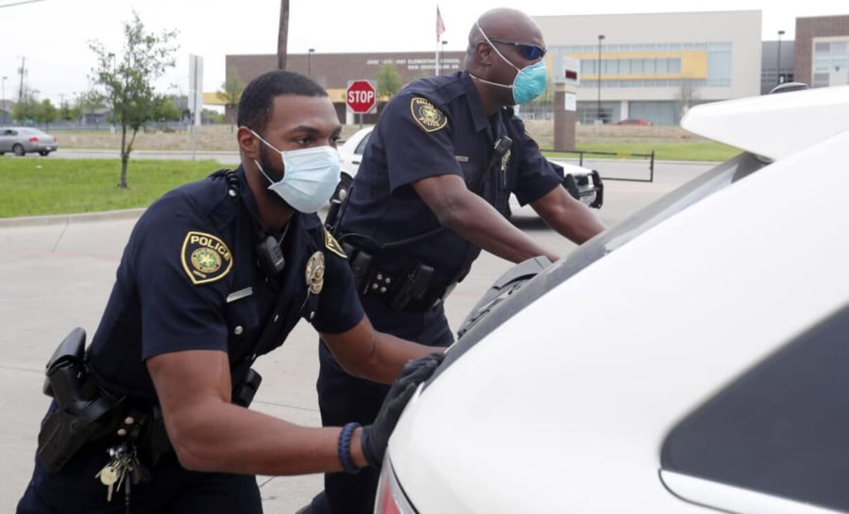 In this April 9, 2020, photo, amid concerns of the spread of COVID-19, Dallas ISD police officers Mylon Taylor, left, and Gary Pierre push a car that ran out of gas while waiting in line for the weekly school meal pick up for students in Dallas. The coronavirus pandemic that has crippled big-box retailers and mom and pop shops worldwide may be making a dent in illicit business, too.