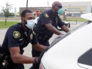 In this April 9, 2020, photo, amid concerns of the spread of COVID-19, Dallas ISD police officers Mylon Taylor, left, and Gary Pierre push a car that ran out of gas while waiting in line for the weekly school meal pick up for students in Dallas. The coronavirus pandemic that has crippled big-box retailers and mom and pop shops worldwide may be making a dent in illicit business, too.